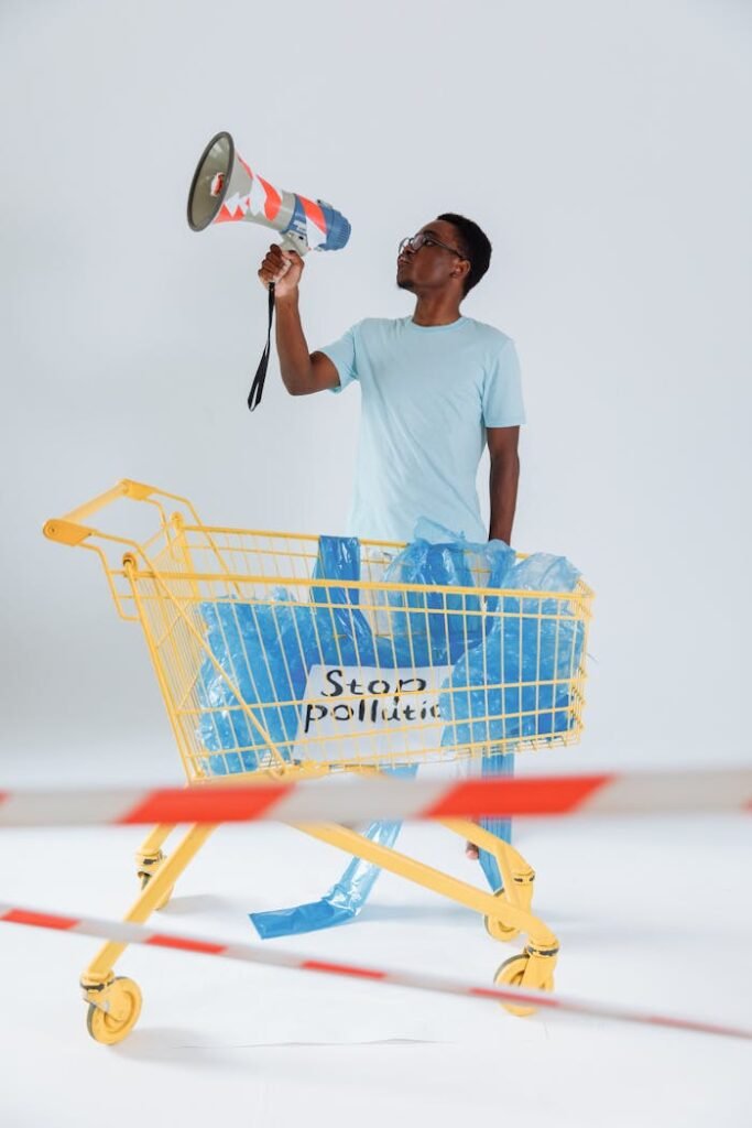 Adult male stands in shopping cart with 'Stop Pollution' sign, holding megaphone.